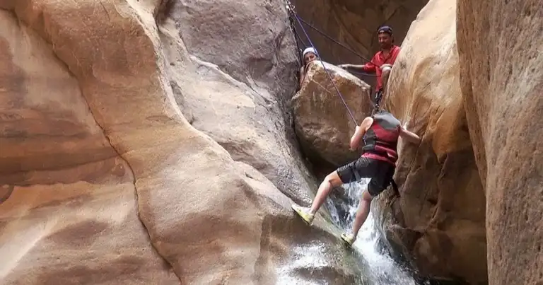 Persona haciendo rappel en cañón estrecho entre rocas de piedra erosionada