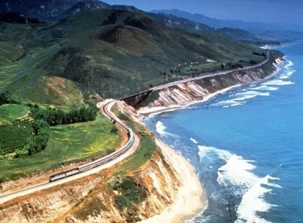 Vías de tren serpentean por acantilados costeros y playas arenosas