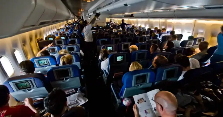 Interior de cabina de avión lleno de pasajeros en asientos azules