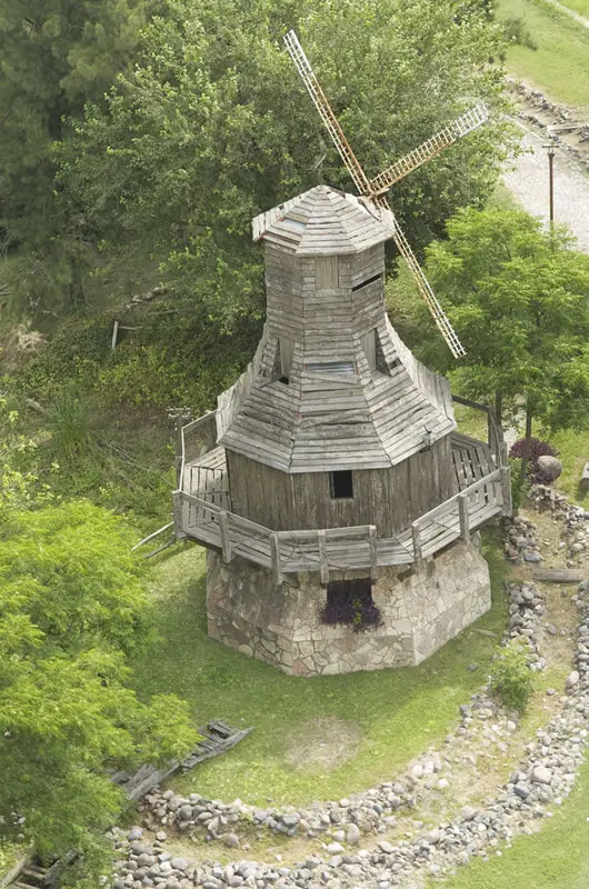 Molino de viento tradicional de madera en campo verde rodeado de árboles