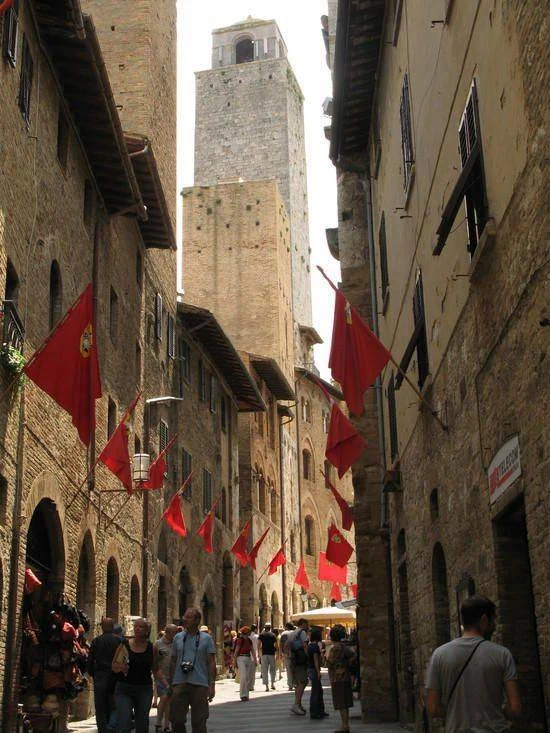 Calle medieval con torres altas y banderas rojas, San Gimignano