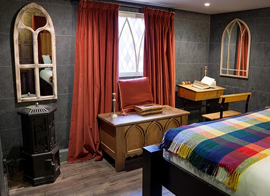 Habitación temática con decoración medieval, ventanas arqueadas, cortinas rojo oscuro y chimenea