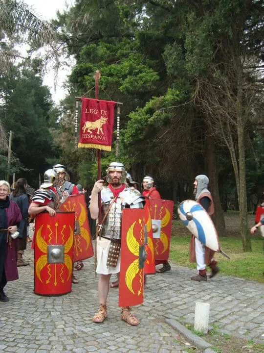 Personas en traje romano rojo con escudos marchando en procesión histórica