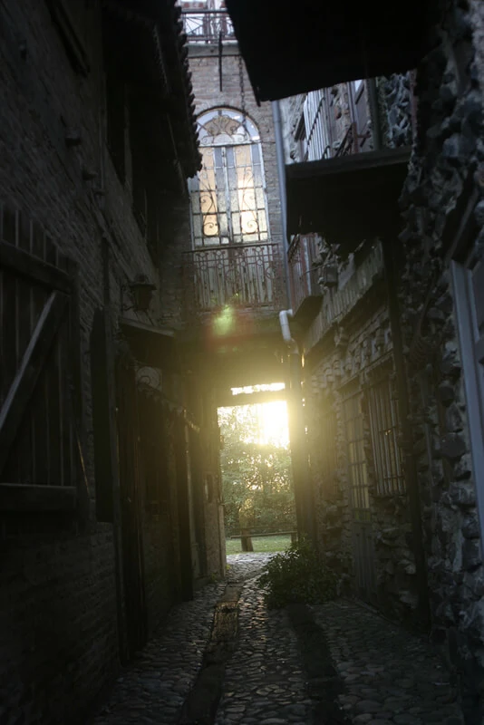 Callejón oscuro de piedra entre edificios históricos con luz al fondo