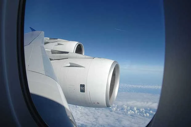 Ventanilla de avión mostrando motor y ala contra cielo nublado