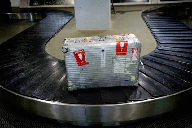 Maleta gris con etiquetas en banda transportadora de aeropuerto