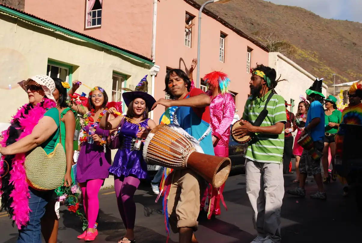 Grupo de personas disfrazadas y con colores vivos desfilan por una calle, una de ellas toca un tambor