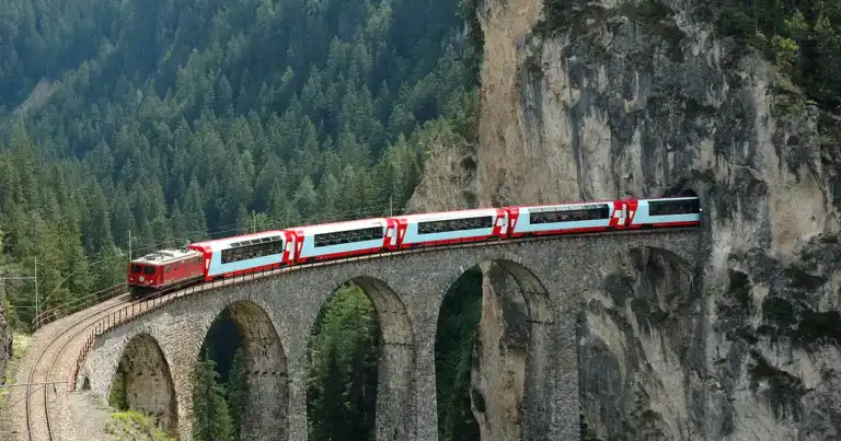 Tren rojo cruzando viaducto arqueado en montaña boscosa de Suiza
