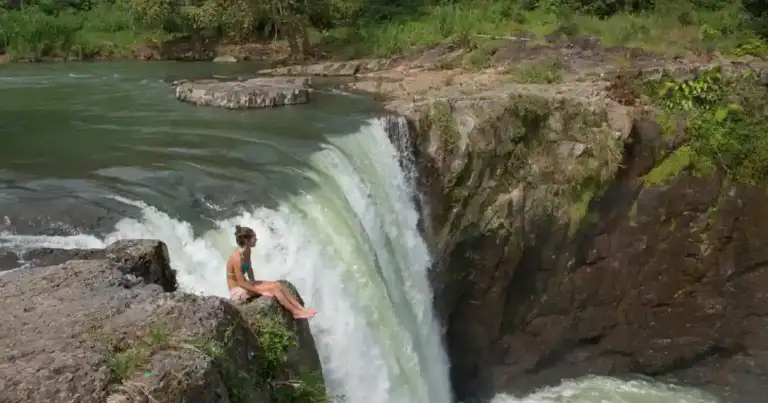 Cascada tropical cayendo desde acantilado en selva verde con personas abajo