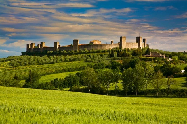 Pueblo amurallado con torres sobre una colina rodeada de olivos y campos verdes