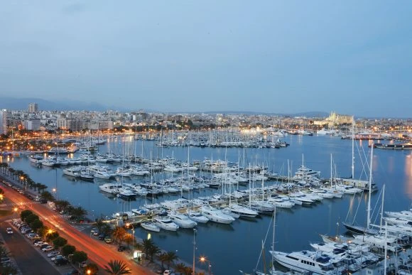 Marina deportiva al anochecer con barcos y luces de la ciudad de fondo