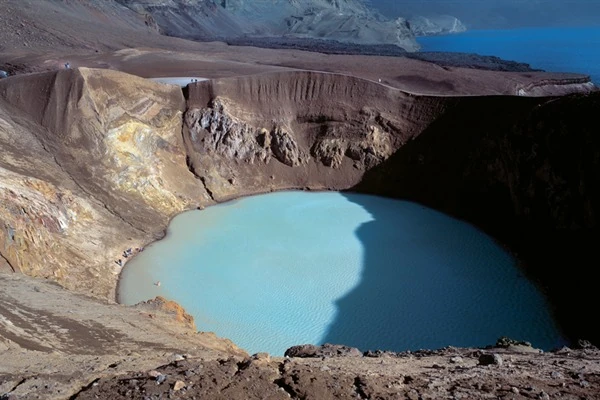 Cráter volcánico con agua cristalina azul turquesa rodeado de tierra árida