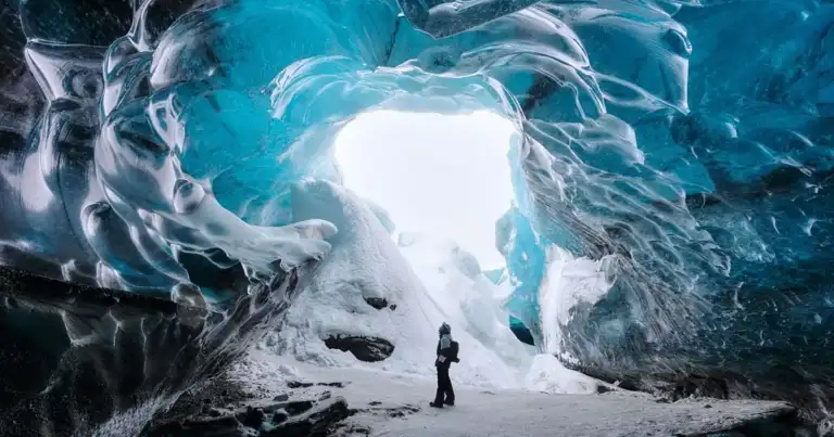 Persona de pie dentro de cueva de hielo azul cristalino en Islandia