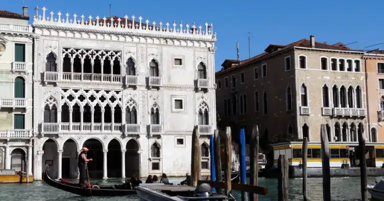 Palacio venetocon fachada blanca ornamentada en canal con góndola azul
