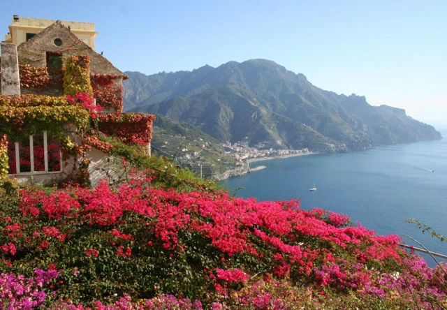Casa color arena con flores fucsia y vista a costa montañosa