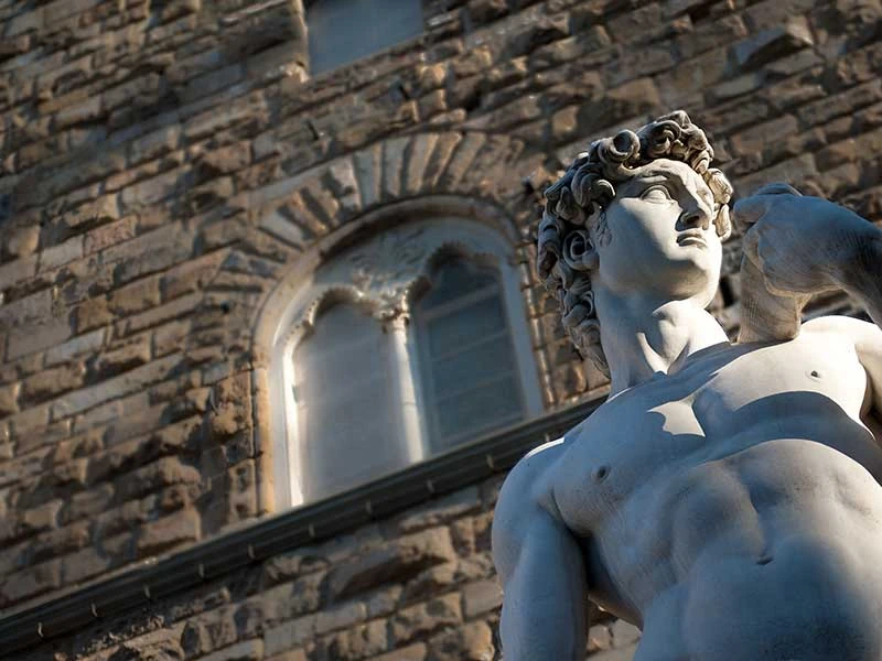 Busto de mármol blanco de escultura clásica frente a edificio medieval de piedra