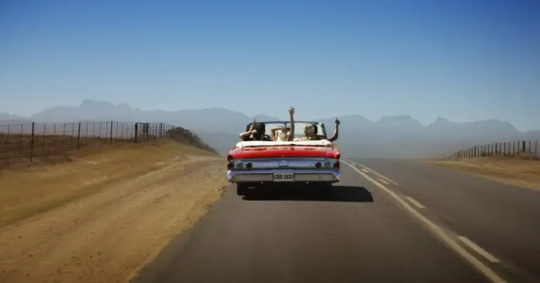grupo de jovenes en auto descapotable con mano levantada recorriendo una ruta