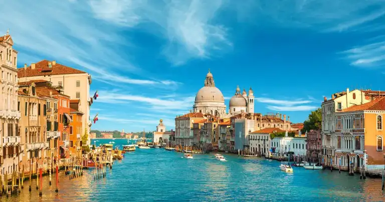 Basílica con cúpula dorada reflejada en canal de agua azul en Venecia