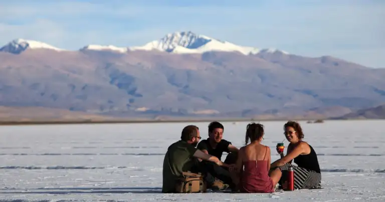 Cuatro personas sentadas en un salar, con montañas nevadas al fondo