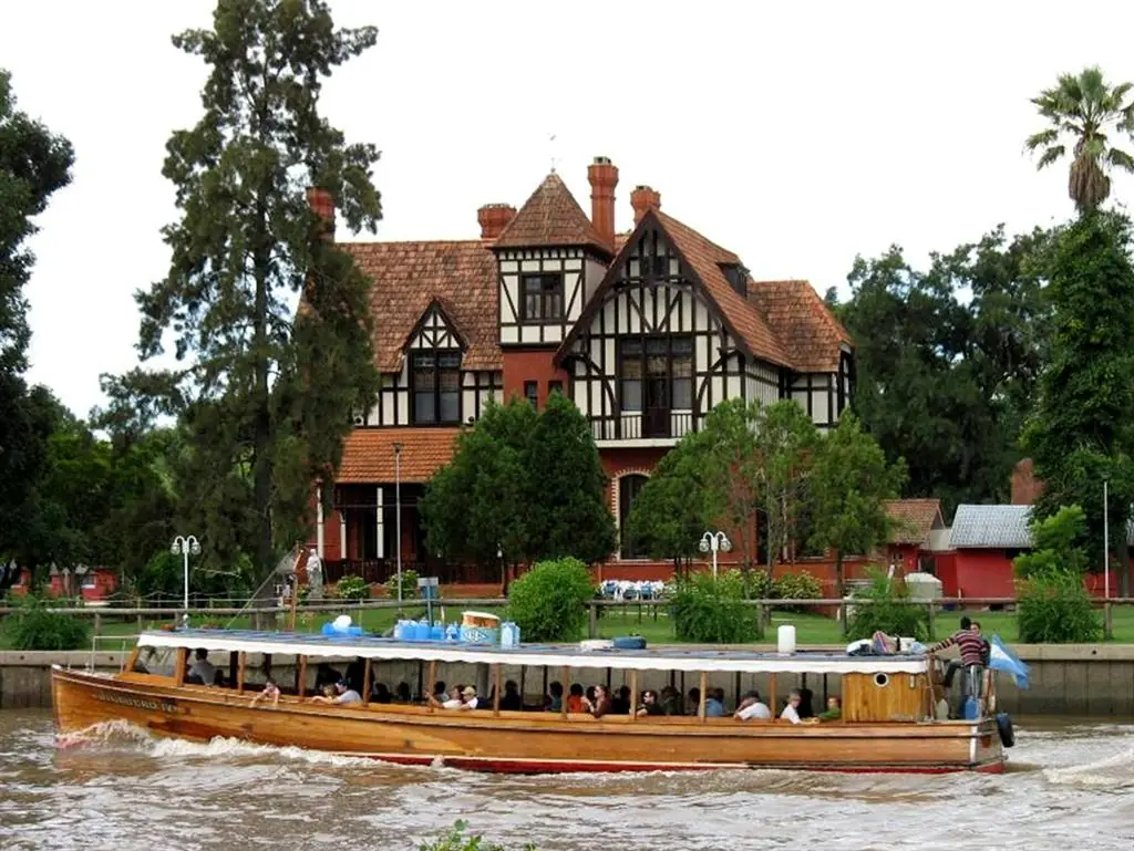 Edificio victoriano junto a río con embarcación turística cargada de pasajeros