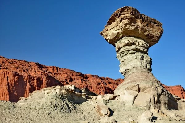 Roca con forma de hongo en paisaje árido con montañas rojas de fondo