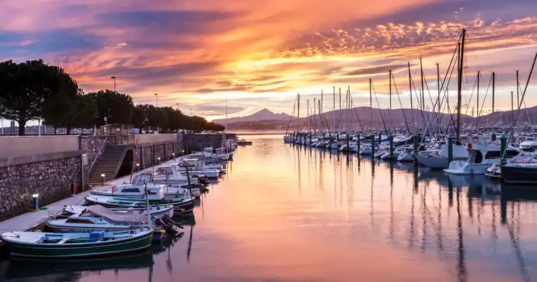 Puerto con barcos reflejados en agua al atardecer en tonos dorados y rosados