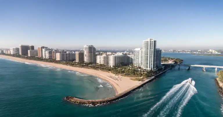 Vista aérea de playa de arena blanca entre rascacielos y océano turquesa