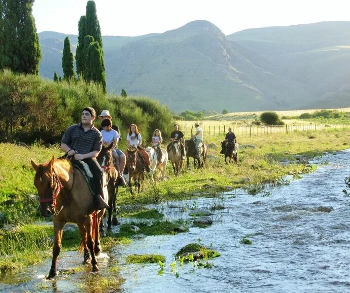 Grupo cabalgando a través de arroyo en paisaje montañoso