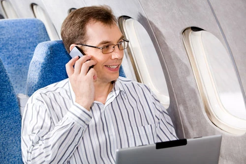 Pasajero en asiento de avión usando teléfono celular y laptop