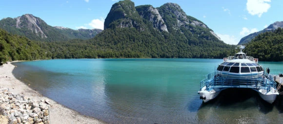 Embarcación turística en el Lago Nahuel Huapi rodeado de montañas y bosques patagónicos, en Villa La Angostura, Argentina