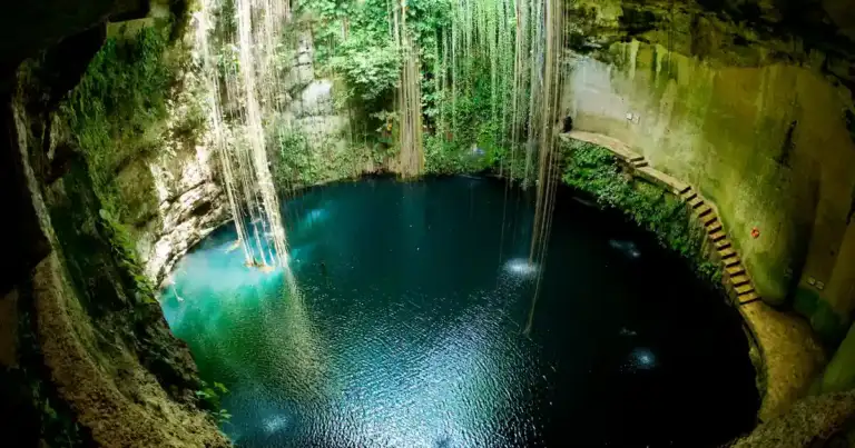 Cenote subterráneo lleno de agua turquesa con techo rocoso e iluminación