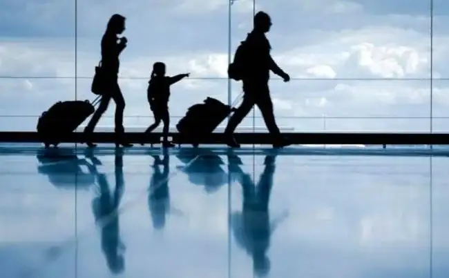 Siluetas de viajeros con equipaje caminando en terminal de aeropuerto reflejadas