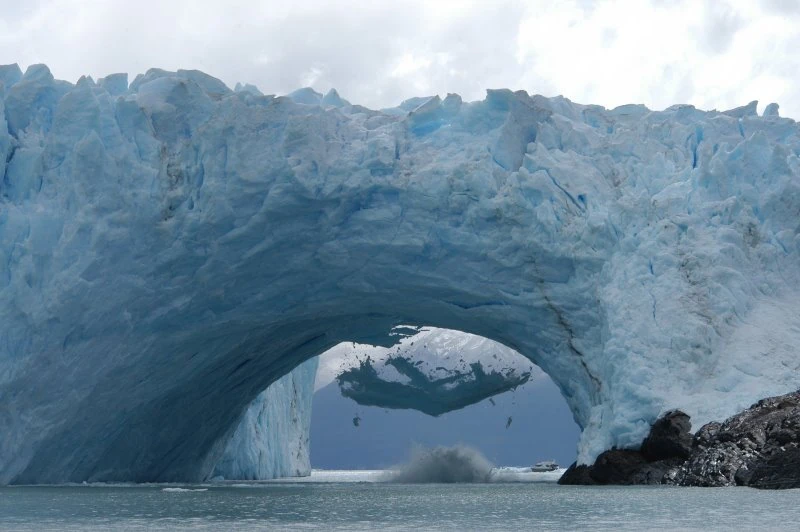 Glaciar blanco con arco de hielo sobre agua y montañas nevadas al fondo