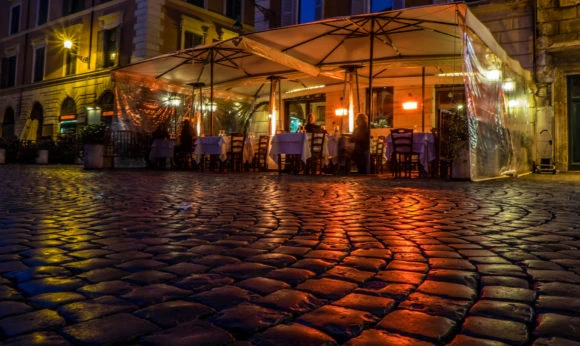Plaza empedrada de noche con mesas de restaurante y edificios históricos