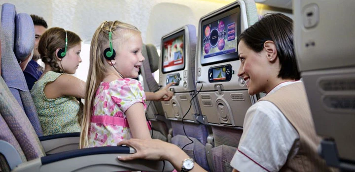 Pasajeros en cabina de avión con niña observando pantalla de entretenimiento