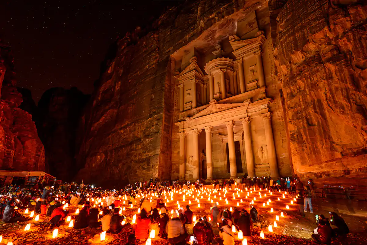 Petra de noche iluminada con luces cálidas, multitud de visitantes frente a fachada de templo tallado