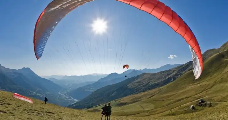 Parapente rojo volando sobre montañas verdes y colinas