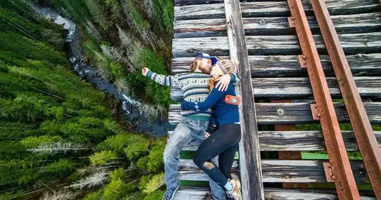 Pareja se abraza y se toma una selfi tumbada sobre las vías de un puente ferroviario de madera sobre un bosque