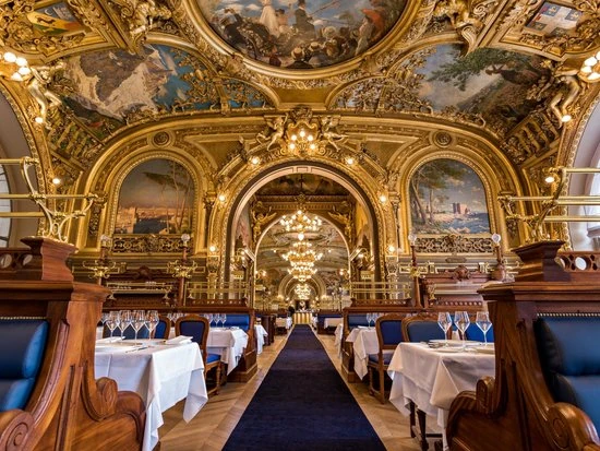 Interior de restaurante lujoso con techo decorado en oro y mesas