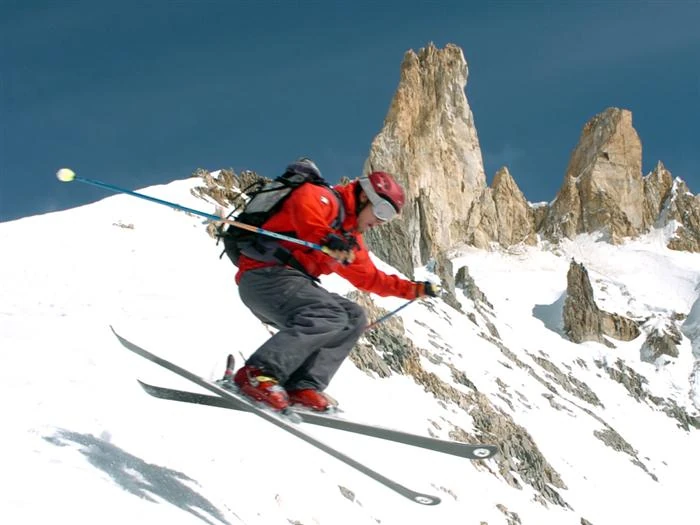 Esquiador en pendiente nevada de Cerro Bayo con picos rocosos
