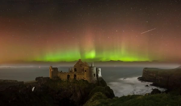Aurora boreal verde sobre ruinas de castillo frente al mar