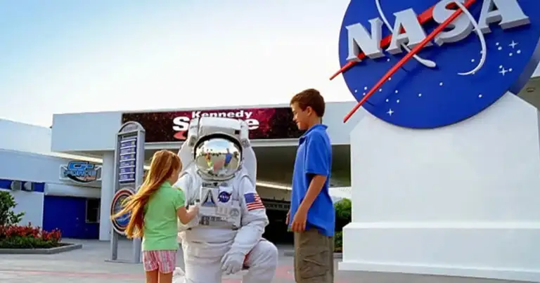 Niños posando con figura de astronauta en parque temático con logo de agencia espacial