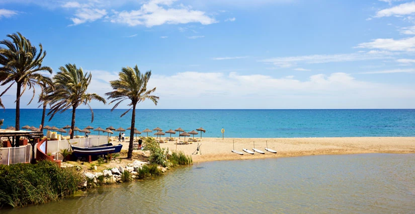 Playa de Marbella con sombrillas de paja sobre la arena en la Costa del Sol
