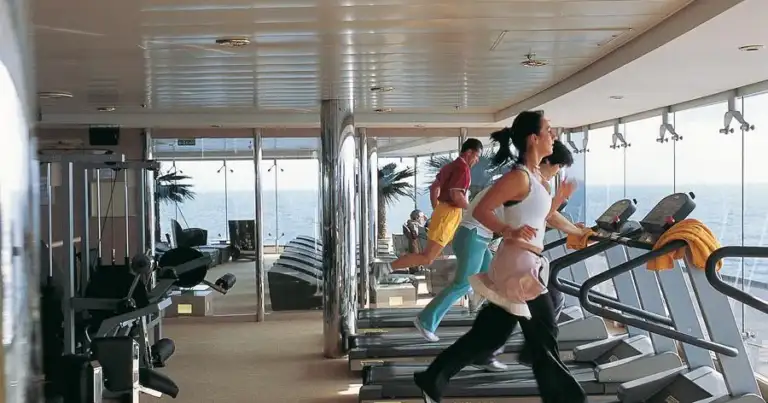 Personas haciendo ejercicio en gimnasio de crucero con máquinas y vista al océano