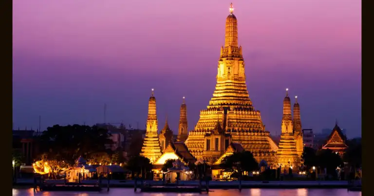 Templo dorado reflejado en agua al atardecer con cielo púrpura y luces iluminadas