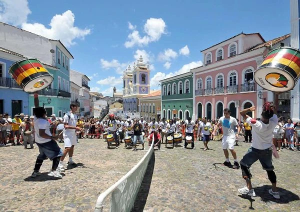 Plaza histórica colonial con iglesia al fondo, edificios de colores pasteles y personas
