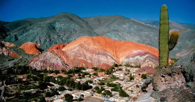 Pueblo de montaña entre cerros rojizos con cactus y vegetación