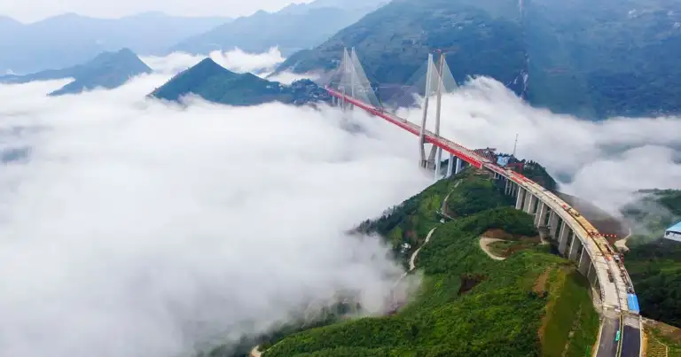 Puente colgante rojo sobre montañas boscosas entre niebla