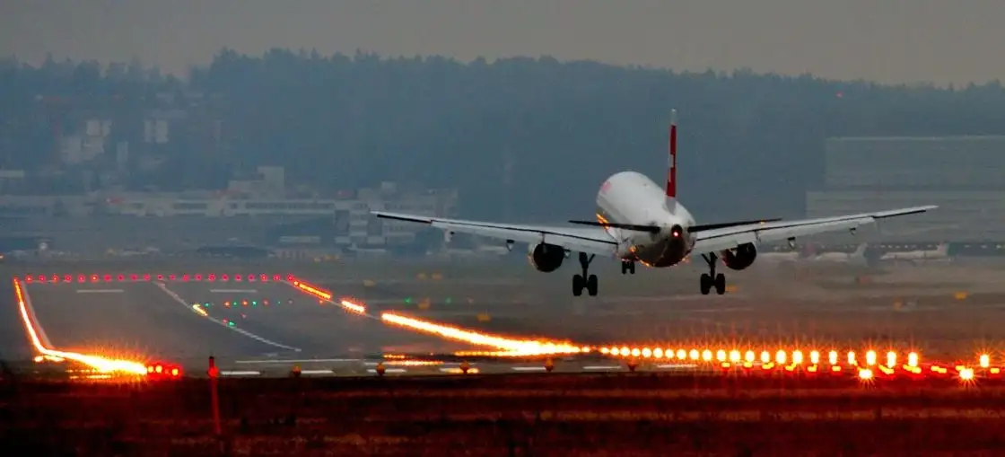 Avión en pista de despegue al atardecer con luces de aterrizaje