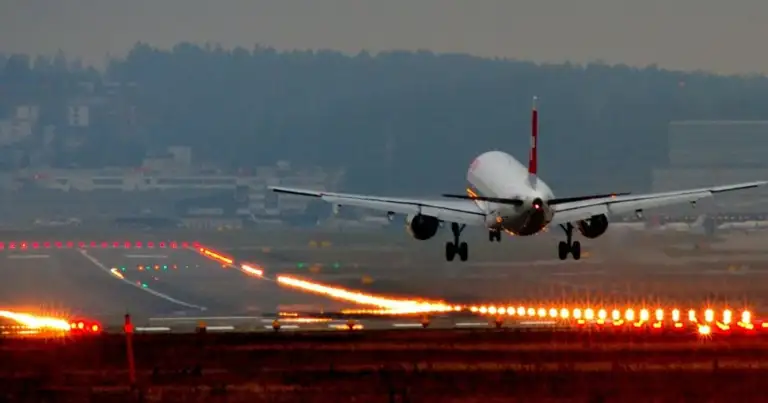 Avión en pista de despegue al atardecer con luces de aterrizaje